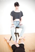 Sitting on stool hands on her thighs stroking cock between her bare feet